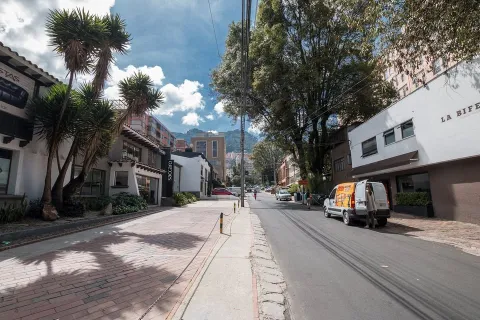 Tree-lined street in Usaquén, Bogotá, featuring restaurants and shops with the Eastern Hills visible in the background.