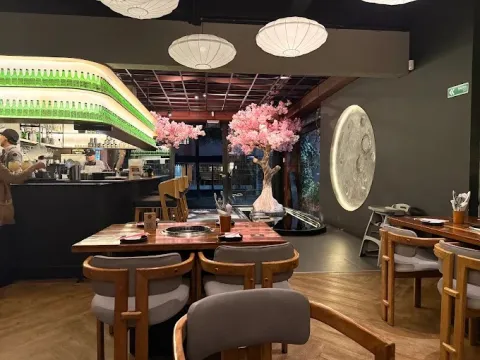 Interior de Gogi con mesas equipadas con parrillas empotradas, barra de bebidas, iluminación cálida y decoración de inspiración asiática.