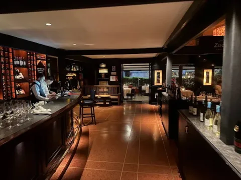 Interior de La Brasserie con ambiente elegante, barra de vinos, iluminación cálida, mobiliario clásico y acceso a una terraza exterior.
