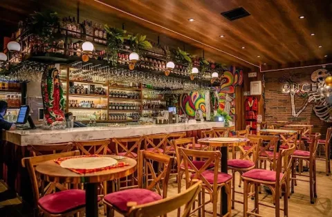 Interior de La Chula con barra de bebidas, mesas de madera, decoración colorida de inspiración mexicana y ambiente festivo.