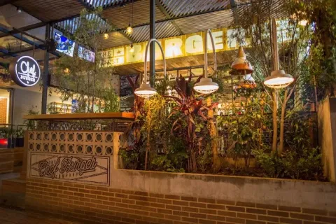 Interior de Chef Burger en la Zona T, con terraza cubierta, vegetación abundante, iluminación cálida y decoración de estilo urbano.