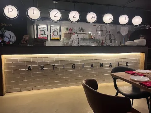 Interior de Pizzardi Artigianale con barra de atención, horno y cocina a la vista, decoración contemporánea y mesas dispuestas para los comensales.