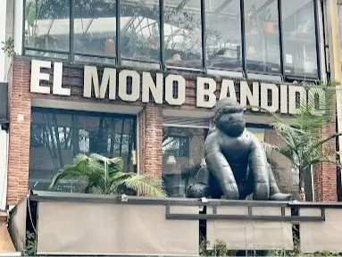 Fachada de El Mono Bandido, con su letrero distintivo, amplios ventanales, vegetación y una escultura de mono en la entrada.