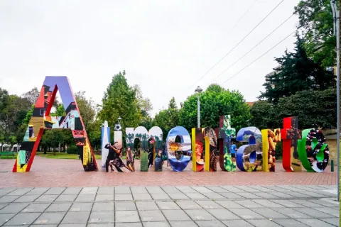 Letras gigantes y coloridas de “Alimentarte” instaladas en un parque de Bogotá, rodeadas de árboles y zonas verdes.