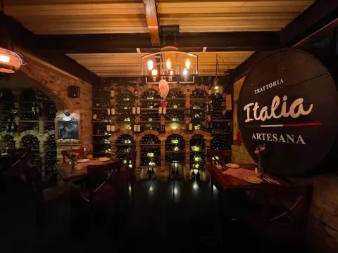 Interior de Italia Artesana, con ambiente rústico e íntimo, paredes de ladrillo, mesas de madera y una amplia cava de vinos.