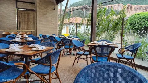 Terraza de La Mar con mesas dispuestas para comensales, sillas de color azul, abundante vegetación y vista a un entorno natural.