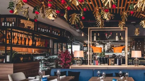 Interior de Seratta Gourmand Market con ambiente elegante, mesas dispuestas para comensales, exhibición de charcutería y vinos, y decoración sofisticada con flores y elementos naturales.
