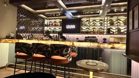 Interior de Izumi con barra de sushi, iluminación cálida, detalles decorativos de inspiración japonesa y mobiliario elegante.