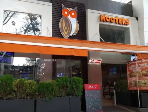 Fachada de Hooters Zona T, con el letrero del restaurante, logotipo de búho, terraza exterior y vegetación en la entrada.