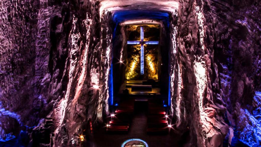 Catedral de Sal de Zipaquirá en interior de caverna con luces rosada y azul y al fondo una cruz azul con luces amarillas.