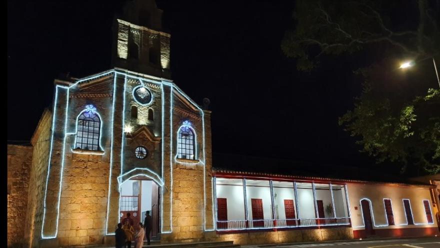  Iglesia Divino Salvador - Sopó, fachada de noche en Navidad con luces alrededor de ventanas y puerta. Grupo de personas al frente conversando. 