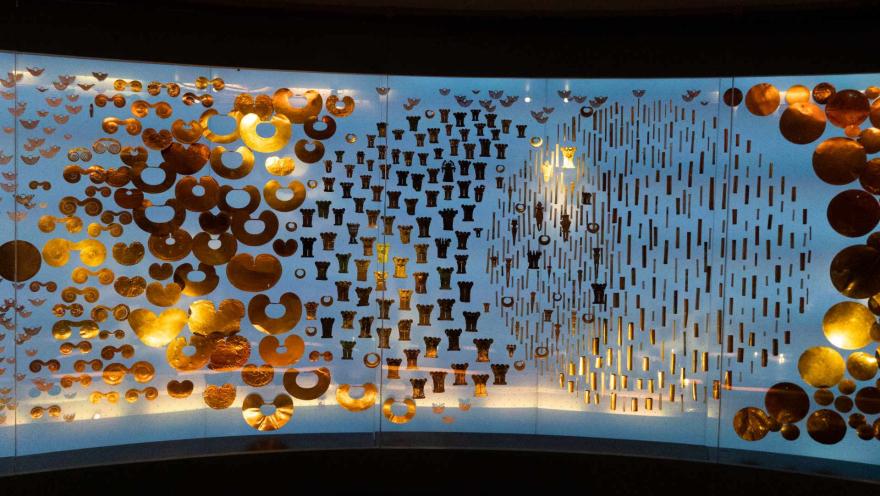 Museo del Oro con vitrina fondo azul con objetos de oro como cadenas, brazaletes narigueras, aretes y otras obras de orfebrería precolombina. estan ordenadas como simulando una luna y un sol.