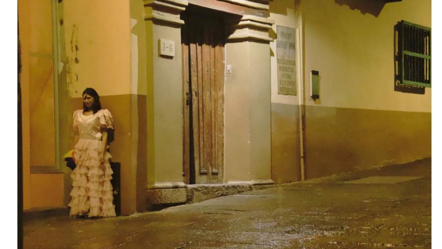  Mujer con cara de demonio y vestida con ropa antigua, detrás de una pared en una calle desolada.