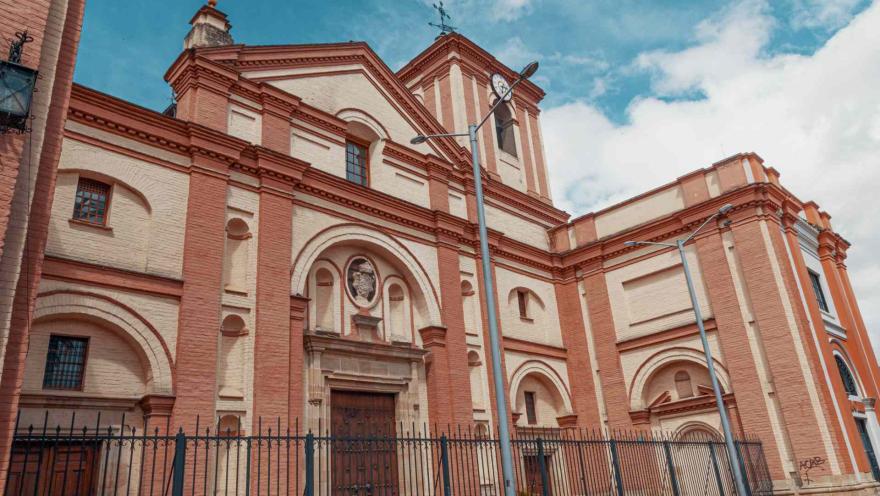 Iglesia San Ignacio fachada completa de lado con un poste eléctrico al frente y el cielo azul con algunas nubes.