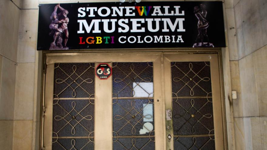 Museo Lgbti primer plano fachada con puerta metálica dorada y aviso en colores que dice Stonewall Museum LGBTI Colombia. El aviso está decorado con imágenes de figuras talladas desnudas y abrazadas.