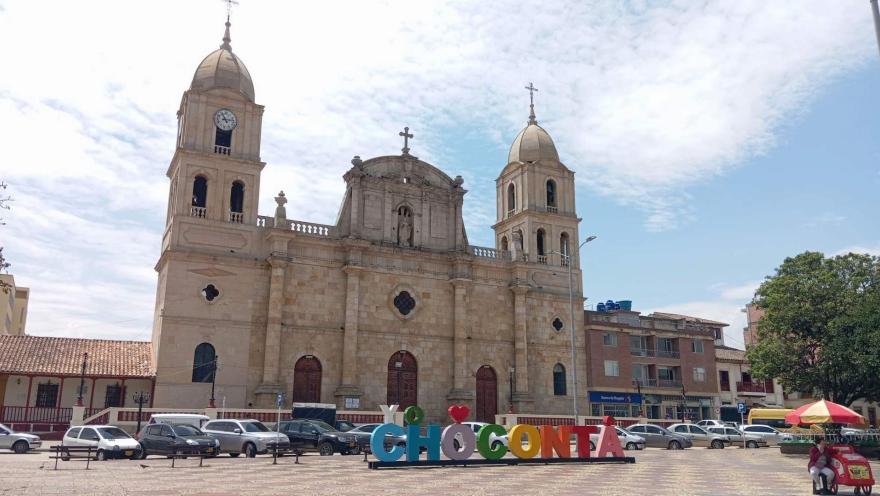 Parroquia Nuestra Señora de la Salud - Chocontá, plano general fachada de día con el cielo azul y algunos autos al frente con la gigantografía del del nombre Chocontá.