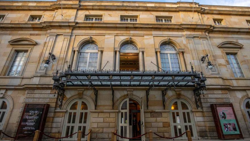Teatro Colón, general view of the façade with the first and second-floor doors open. Neoclassical architecture with ornamental and functional details in carved stone, featuring its horseshoe shape. On both the left and right sides, there is a promotional sign.