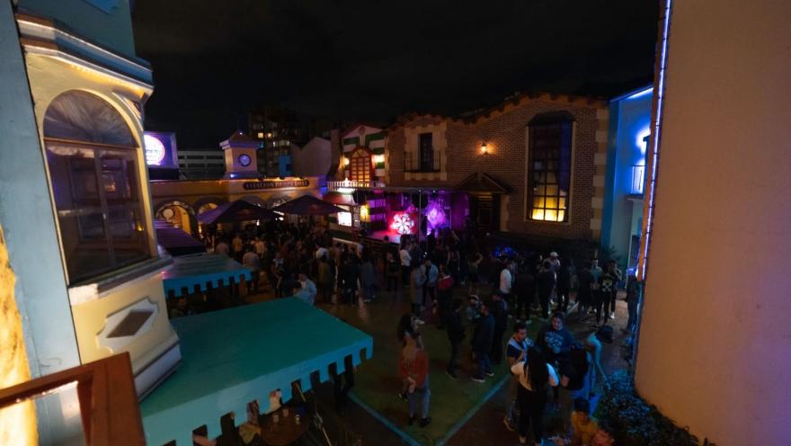 Theatron plazoleta interna de noche con fachadas de castillos y personas conversando.