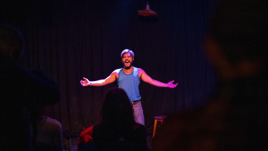 Barraca Teatro con artista hombre joven en tarima sonriendo ante un público.