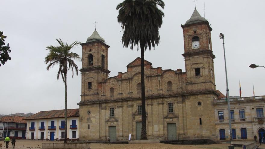  Catedral Santísima Trinidad y San Antonio de Padua, fachada frente de día cielo gris y un par de palmas a los costados. Dos personas caminan al frente.