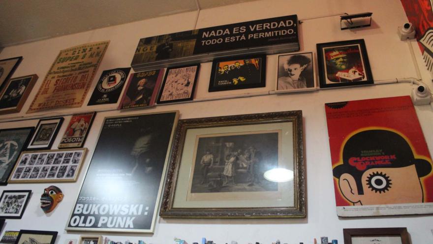Librería La Valija de Fuego con una pared blanca repleta de cuadros de artístas y fiches de películas. También hay una repisa repleta de libros.