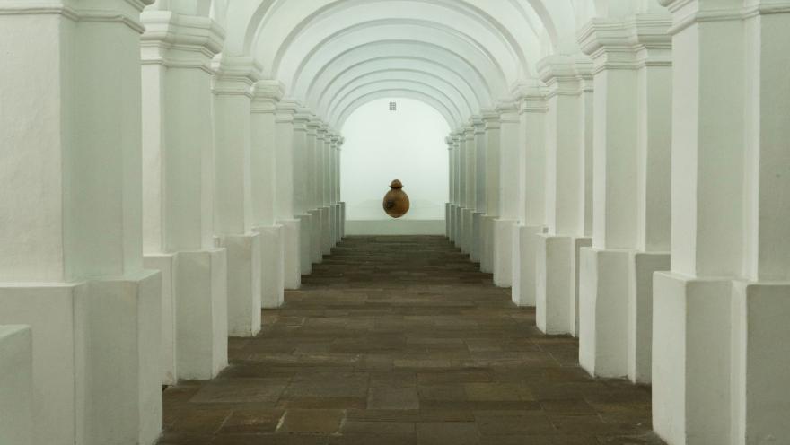 Museo Nacional de Colombia en el interior pasadizo blanco con columnas que forman óvalos. Al final se observa una vasija redonda de barro.   