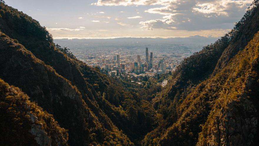 Cerros Orientales con la ciudad vista entre dos montañas tupidas de árboles. El cielo es gris con nubes.