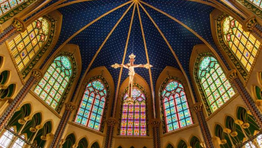 Santuario Nuestra Señora de Fátima - Tocancipá interior con vista desde abajo de la cúpula azul con estrellas, ventanales en óvalos con vitrales. Destaca al frente un Cristo crucificado que cuelga del techo. 
