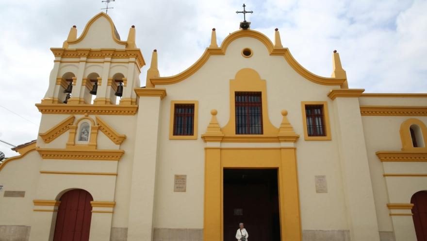 Santuario Nuestra Señora de la Salud - Bojacá y la fachada de frente con una mujer adulta en la puerta que está cerrada.