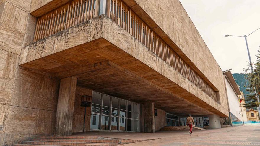 Biblioteca Luis Ángel Arango parte moderna con fachada en baldosa carmelita. Un hombre camina al frente.