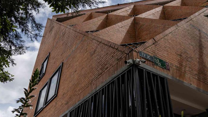 Chapinero con fachada de edificio con forma geométrica y en ladrillo con dos ventanas cuadradas y rejas metálicas color negro. A la izquierda hay unas ramas de árbol.