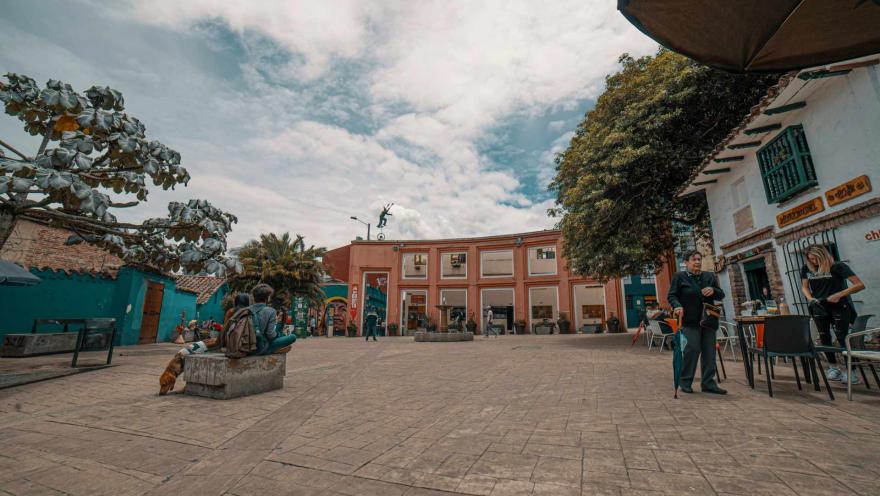  Plazoleta del Chorro de Quevedo en plano genral con personas departiendo. El cielo es azul con nubes.