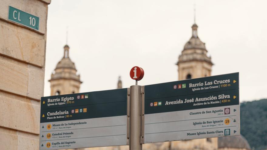 Plaza de Bolívar con primer plano de señal turistica y aviso de calle 10 en pared y de fondo borrosa las torres de la Catedral Primada.