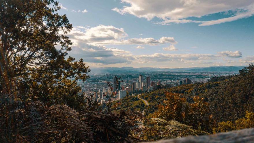 Sendero Cerro Monserrate con vista de la ciudad desde la montaña con árboles frondosos y el cielo azul con algunas nubes.