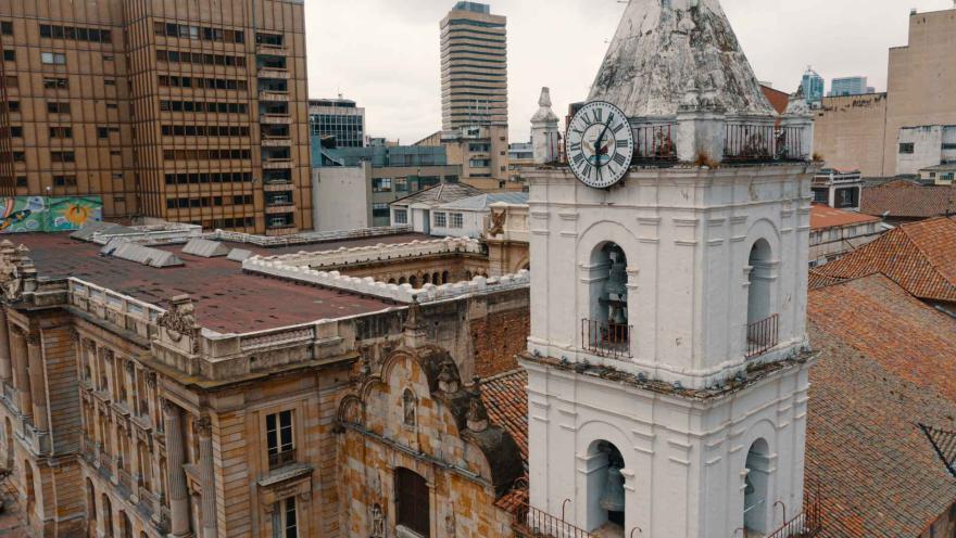 Iglesia San Francisco su blanca torre del reloj y campanario en primer plano y otros techos de edificaciones contiguas.