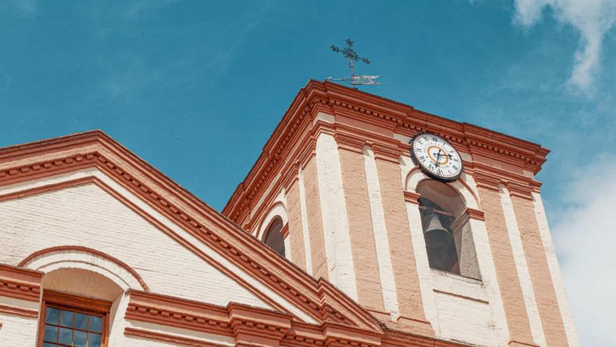 Iglesia San Ignacio en primer plano en contrapicado de la torre del reloj y cruz de metal. El cielo es azul.