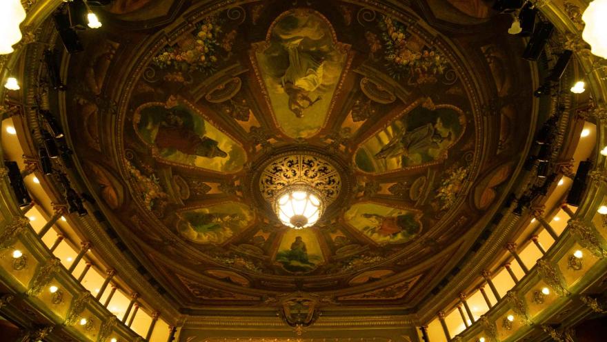 Teatro Colón, image of the dome seen from below. The paintings, the windows around the circle, and a lit lamp embedded in the very center stand out. 