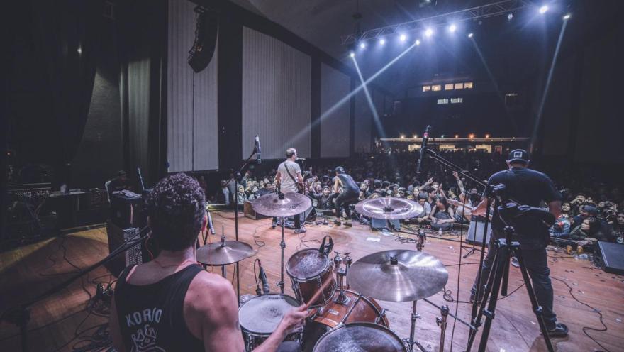  Auditorio Mayor al interior en tarima con grupo musical de rock vistos por un centenar de personas que bailan.