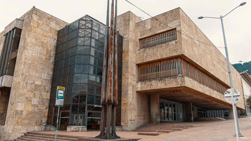  Biblioteca Luis Ángel Arango parte moderna con fachada en baldosa carmelita y puerta grande en vidrio y una monumento metálico. Hay un paradero de SITP.