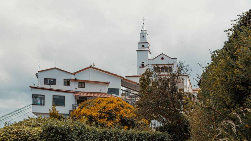 Monserrate Hill, side view of the church in a wide shot surrounded by vegetation and trees. The gray sky is overcast with clouds.