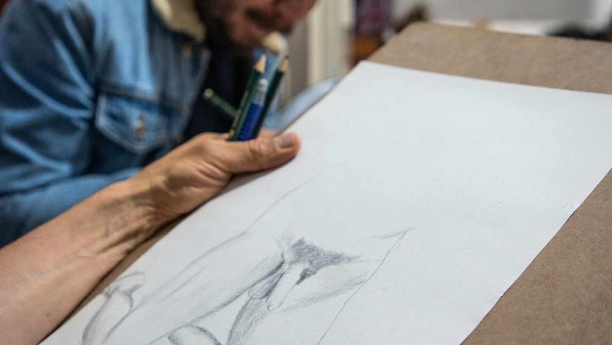  Chucuy Club con un dibujo de un pene en una hoja de papel, manos de dibujante en primer plano y de fondo un hombre jóven parece que dibujando.