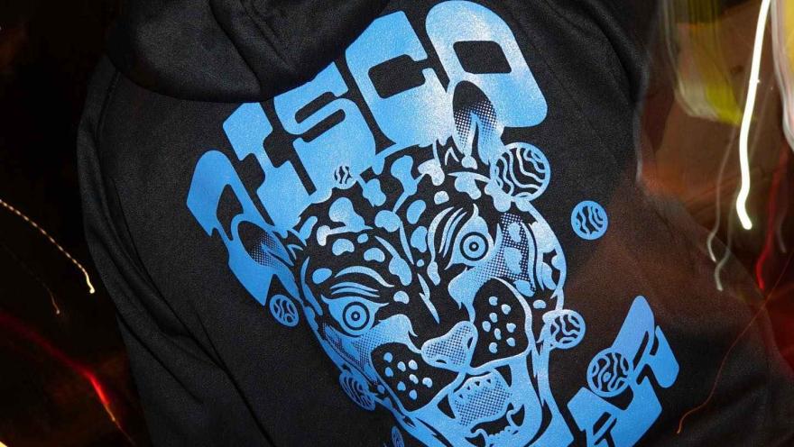 Disco Jaguar con chaqueta con capucha negra y el logo en letras azules claras de Disco Jaguar y un rostro de jaguar.