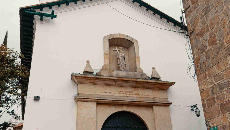 Iglesia de La Veracruz su fachada principal con puerta de marco en círculo, de color verde y que está cerrada. En la vista de abajo hacia arriba se nota un cielo blanco.  