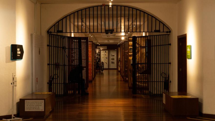 Museo Nacional de Colombia al interior pasadizo con vitrinas de madera a lado y lado, piso en madera y separado por una puerta de hierro semi abierta.