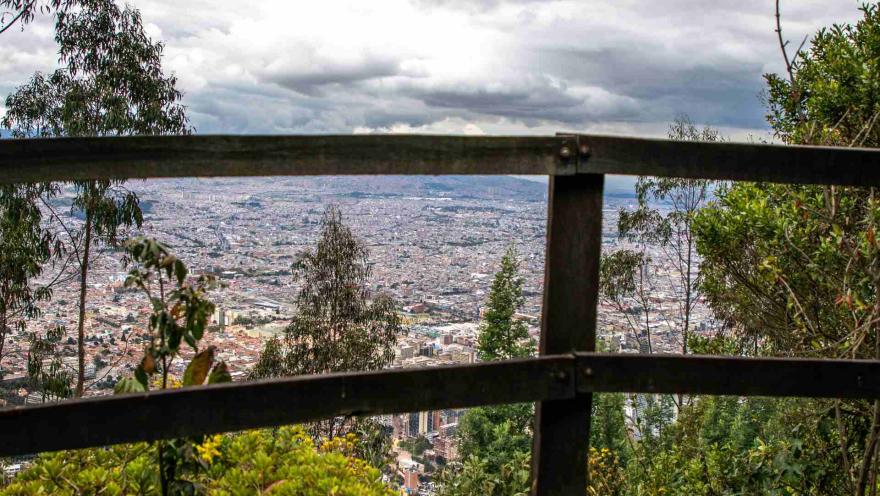 Sendero Cerro Monserrate con vista de la ciudad desde una de las cercas de madera y árboles abajo en la montaña. El cielo es gris.