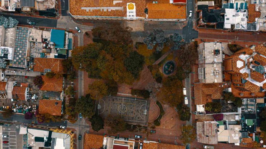 Plaza de Usaquén e plano general en dron desde el cielo en el que se ven los techos de las casas, la cancha de microfútbol, los frondosos árboles y las calles. No hay personas.