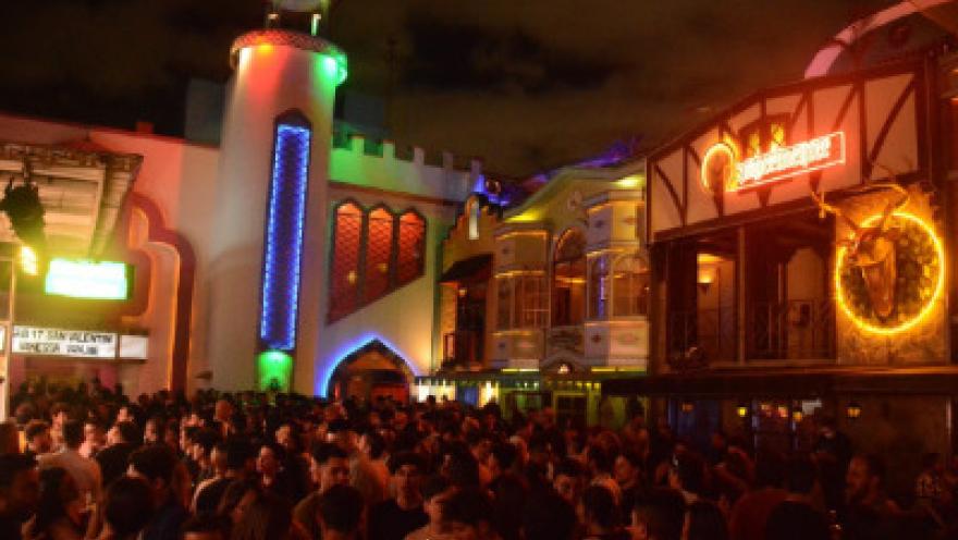 Theatron de noche intrior plazoleta llena de personas alrededor de fachadas iluminadas.