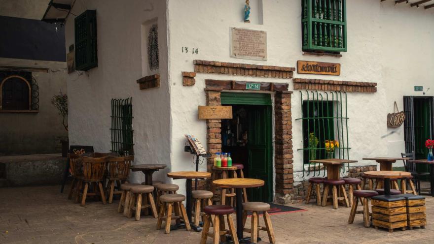 Plazoleta del Chorro de Quevedo con casa colonial de dos pisos y fachada blanca dispuesta como restaurante con mesas y sillas afuera.