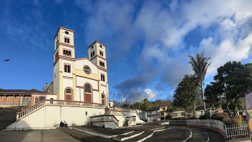  Iglesia Parroquial Nuestra Señora del Rosario - Junin vista desde abajo en la plazoleta rodeada de árboles con dos personas sentadas afuera y un cielo de atardecerazul  con algunas nubes.