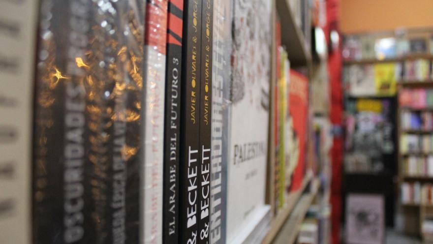  Librería La Valija de Fuego con primer plano de libros ordenados en anaquel y al fondo borroso otro anaquel lleno.